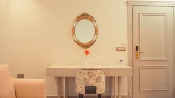A room with a white desk, a chair with floral upholstery, a mirror with an ornate frame, and a closed door.