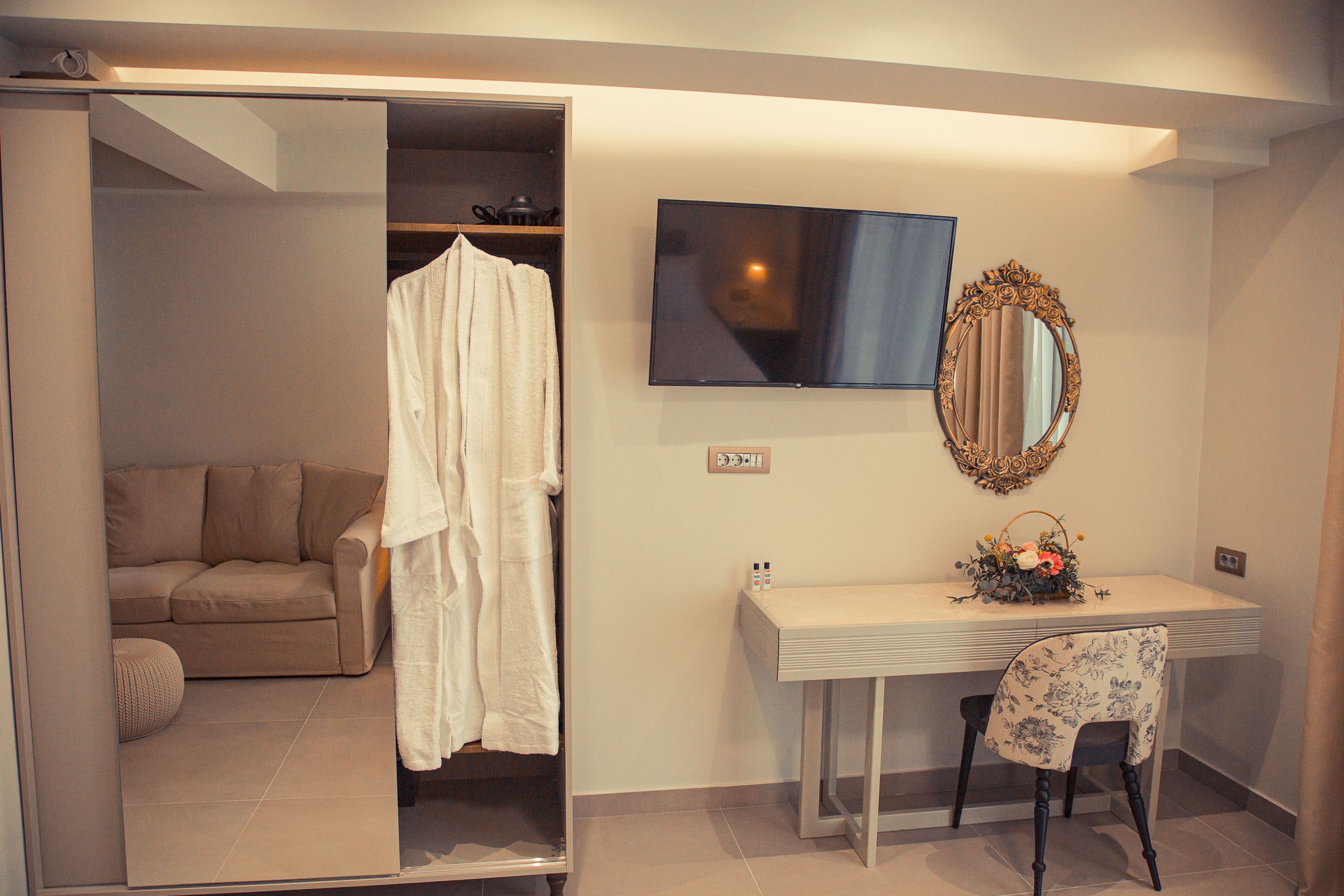 A bedroom with a bed, a vanity with a mirror, a television, and a sofa.