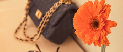 A dark blue handbag with a gold chain strap, a pair of sunglasses, and a single orange flower in a vase.