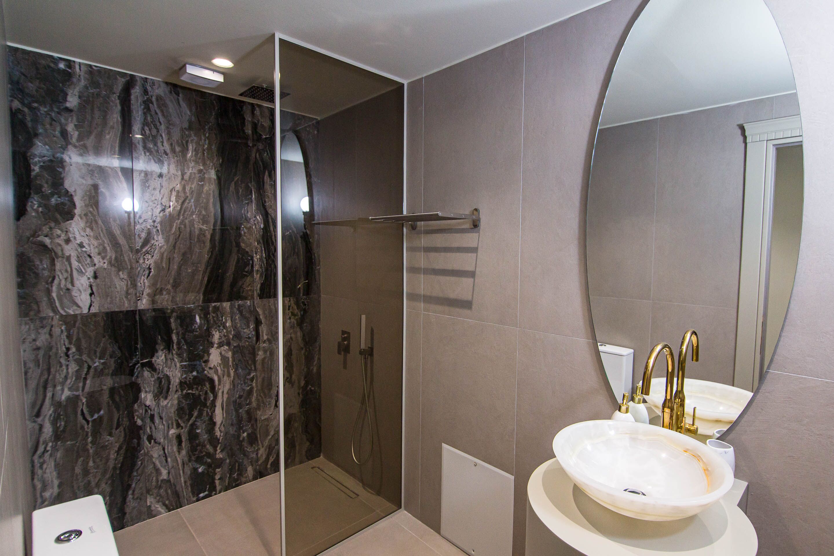 A modern bathroom with a glass-enclosed shower, a white sink with gold fixtures, and marble walls.