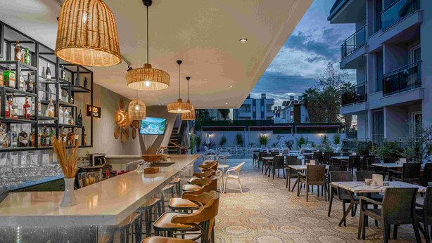 A bar area with a long counter, multiple chairs, and hanging wicker lamps. - A Hotel Side (Manavgat)