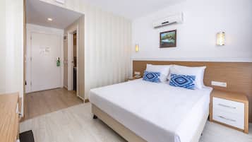 Habitación de hotel con una cama grande, una mesita de noche y un aire acondicionado instalado en la pared, además de una puerta que da a un pasillo.