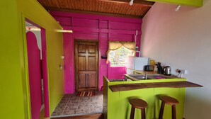 Une cuisine compacte avec une porte en bois, une petite fenêtre avec un rideau, un évier, une cuisinière et deux tabourets.