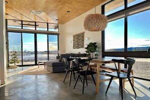 Ein geräumiges Zimmer mit großem Fenster, einem Essbereich mit Stühlen und Tisch sowie einem Sofa.