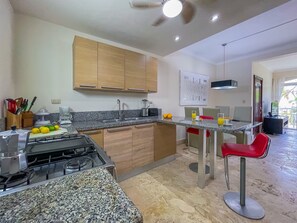 A modern kitchen with granite countertops, wooden cabinets, a gas stove, and a dining area with red chairs.