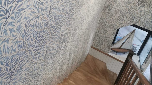 Eine Treppe mit Holzbalken und Geländer, die zu einer Zwischenplattform mit einem Modell eines Segelbootes auf einem Tisch führt.
