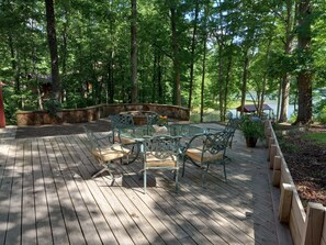 A wooden deck with a glass-top table and metal chairs, surrounded by a stone wall and lush greenery. - Log Cabin/Cottage on Watts Bar Lake (Ten Mile)