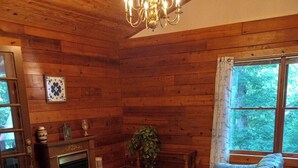 A cozy log cabin interior with a large wooden sofa, a fireplace, and a chandelier. - Log Cabin/Cottage on Watts Bar Lake (Ten Mile)