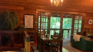 A cozy cabin interior with a wooden dining table, chairs, a chandelier, a green sofa, and a stone wall. - Log Cabin/Cottage on Watts Bar Lake (Ten Mile)
