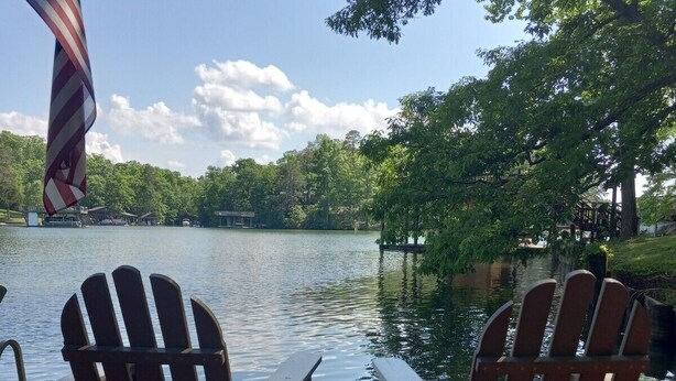 A wooden deck with Adirondack chairs overlooking a lake, a flag, and trees in the background. - Log Cabin/Cottage on Watts Bar Lake (Ten Mile)