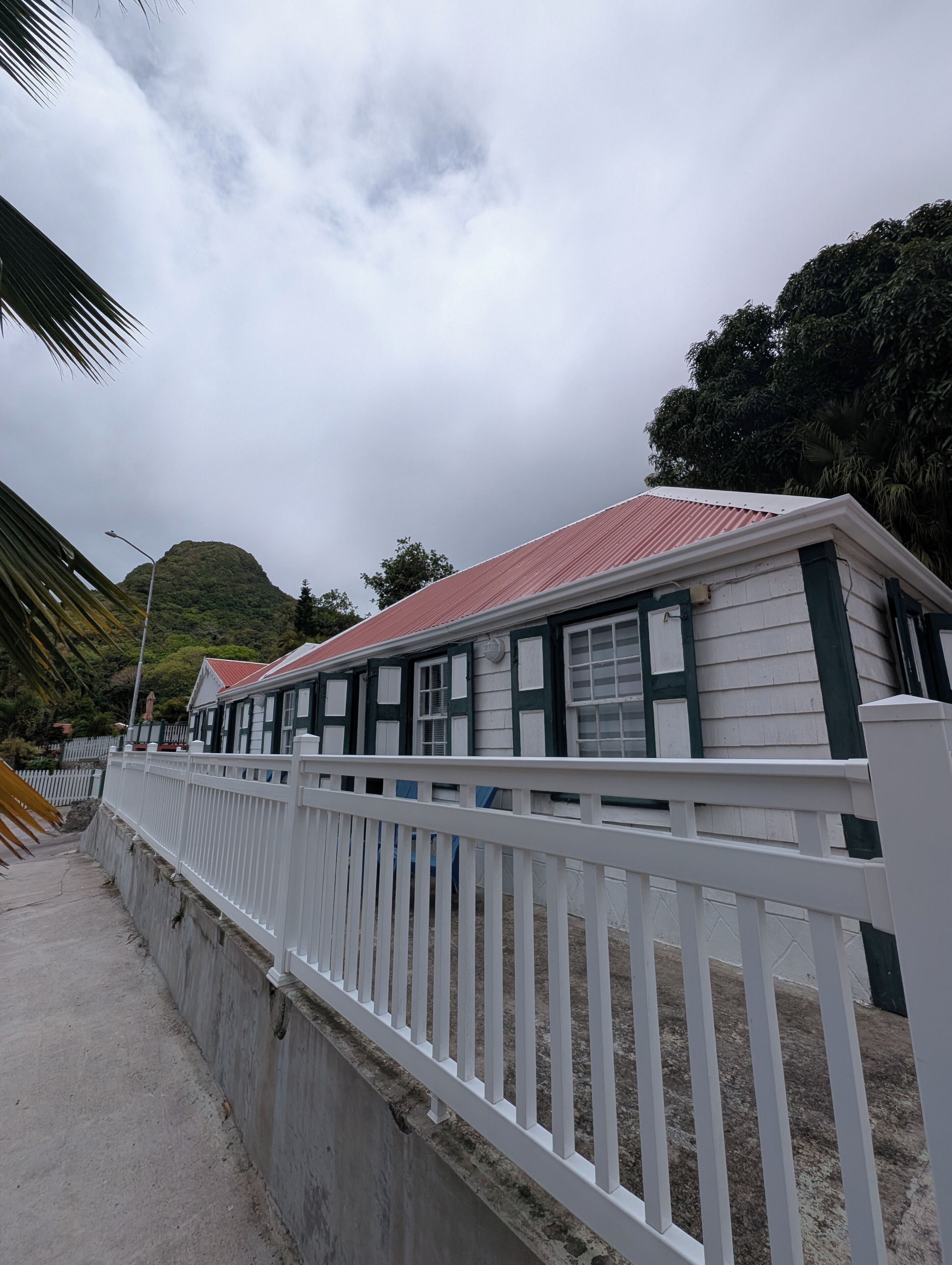 A coastal building with a red roof, white exterior, and a white fence.