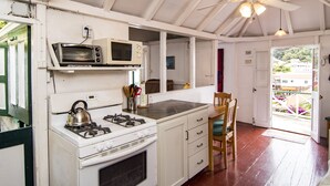 A kitchen with a stove, microwave, and a dining area with a chair. - Historic Saban cottage in Windwardside, all amenities only a 2 minute walk away! (Windward Side)