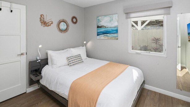 Un dormitorio con cama, mesitas de noche, ventilador de techo, ventana con vistas y adornos en la pared.