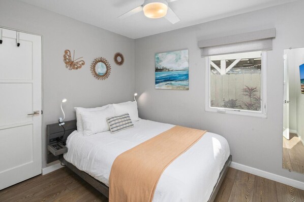 A bedroom with a bed, bedside tables, a ceiling fan, a window with a view, and wall decorations.