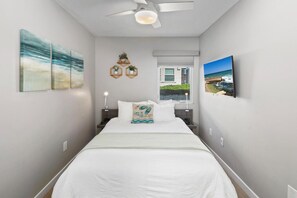 Quarto de hotel com cama, ventilador de teto, janela com vista e obras de arte nas paredes.