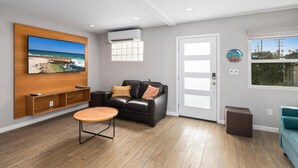 Una sala moderna con un mueble de televisión de madera, un sofá de cuero negro, una mesa de centro redonda y un ventanal con vistas al exterior.