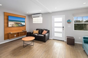 A modern living room with a wooden TV stand, a black leather sofa, a round coffee table, and a large window with a view of the outdoors.