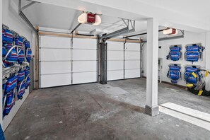 Uma garagem com duas portas grandes, piso de concreto e várias malas azuis e vermelhas penduradas nas paredes.