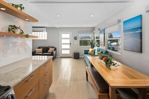 A modern kitchen with wooden cabinets, a marble countertop, and a dining area with a wooden table and bench.