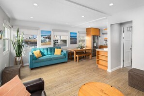 Uma sala de estar moderna com sofá azul, mesa de jantar de madeira e área de cozinha com geladeira.