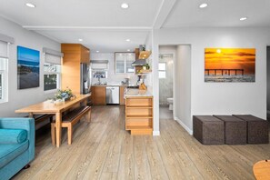 A modern kitchen with wooden cabinets, a dining area with a bench, and a view of the sunset through a window.