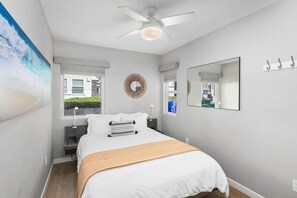 Une chambre à coucher avec un lit, un ventilateur de plafond, une fenêtre et un miroir fixé au mur.