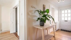 Um corredor com piso de madeira, uma porta branca e um vaso de planta sobre uma pequena mesa.