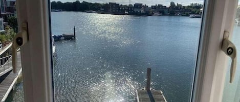 Vista de un lago tranquilo con un muelle que se adentra en el agua, rodeado de edificios y árboles bajo un cielo despejado.