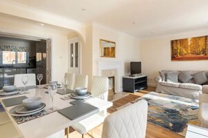 A modern living room with a dining area, a fireplace, and a large painting on the wall.