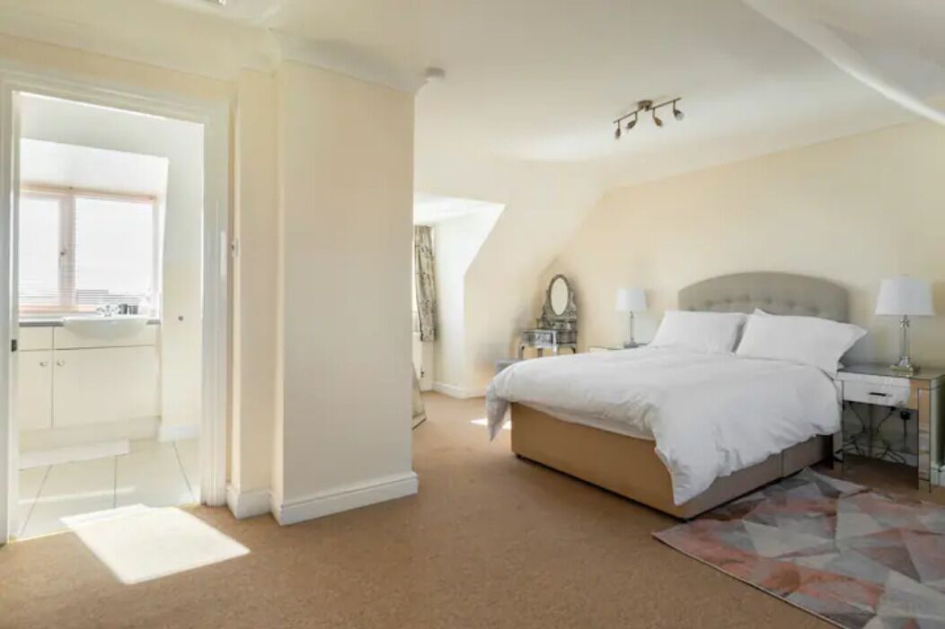 A bedroom with a large bed, bedside tables, a mirror, and a view of the kitchen.