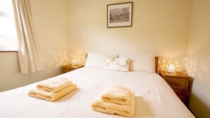 A neatly made bed with two folded towels, a framed picture on the wall, and two bedside lamps. - Family-sized Lake District village house with garden, plus gorgeous walks from the door (Coniston)