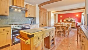 Une cuisine avec des meubles de rangement en bois, une cuisinière et un coin repas comprenant des chaises et une table en bois.