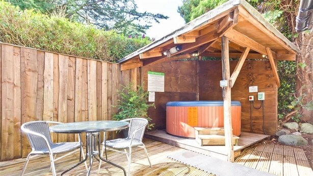 Une terrasse en bois avec un jacuzzi, deux chaises en métal et une table.