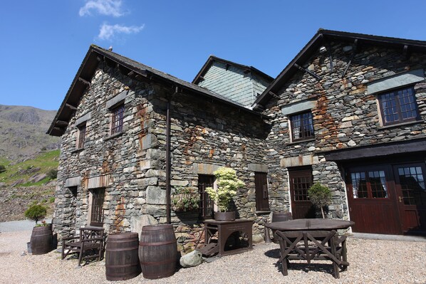 Traditional stone building with a rustic entrance, featuring a wooden door and windows, and a charming outdoor seating area.