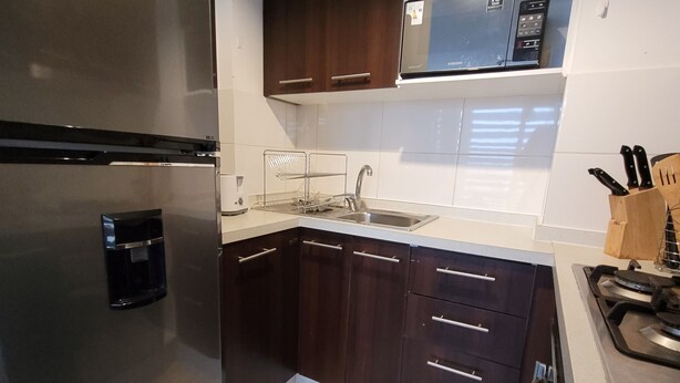 A modern kitchen with dark wooden cabinets, a stainless steel refrigerator, a microwave, and a gas stove. - EXELENTE VISTA AL MAR Y MUY CERCANOS A PLAYAS, CENTRO DE LA CIUDAD. (Valparaíso)