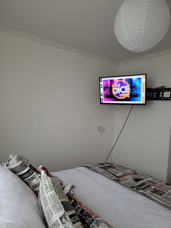 A bedroom with a bed covered in newspaper, a television on the wall, and a white ceiling light. - EXELENTE VISTA AL MAR Y MUY CERCANOS A PLAYAS, CENTRO DE LA CIUDAD. (Valparaíso)