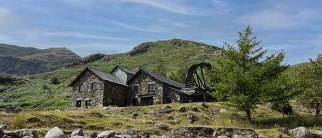 Une maison en pierre avec un moulin à vent, entourée d’un paysage rocheux et de collines.