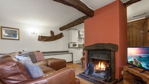 A cozy living room with a fireplace, a leather sofa, and a television on a wooden stand. - Unique mountain cottage for 4 with hot tub and stunning views (Coniston)