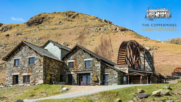 Une charmante maison en pierre dotée d’une roue à eau, située dans un cadre montagneux.