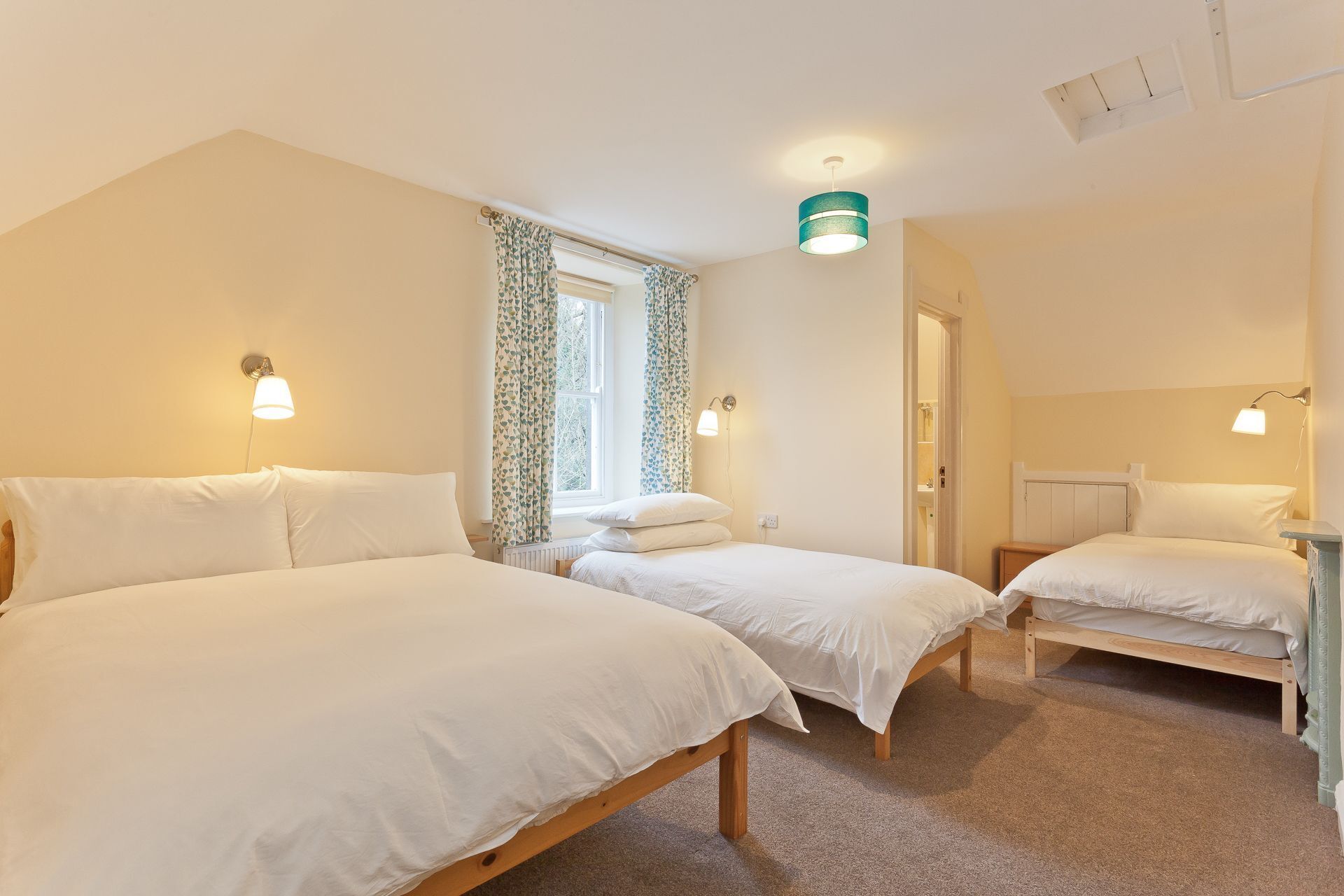 Een slaapkamer met twee eenpersoonsbedden, een raam met gordijnen, een plafondlamp en een deur.