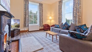 A living room with a fireplace, sofa, and a television. - Large Lake District House in popular village with gorgeous lake views (Coniston)