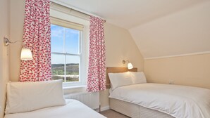 A bedroom with two beds, a window with curtains, a radiator, and a wall-mounted lamp. - Large Lake District House in popular village with gorgeous lake views (Coniston)