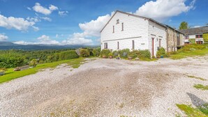 Ein weißes Steinhaus mit Kiesauffahrt, umgeben von Grünflächen und mit einem schönen Blick auf die Berge.