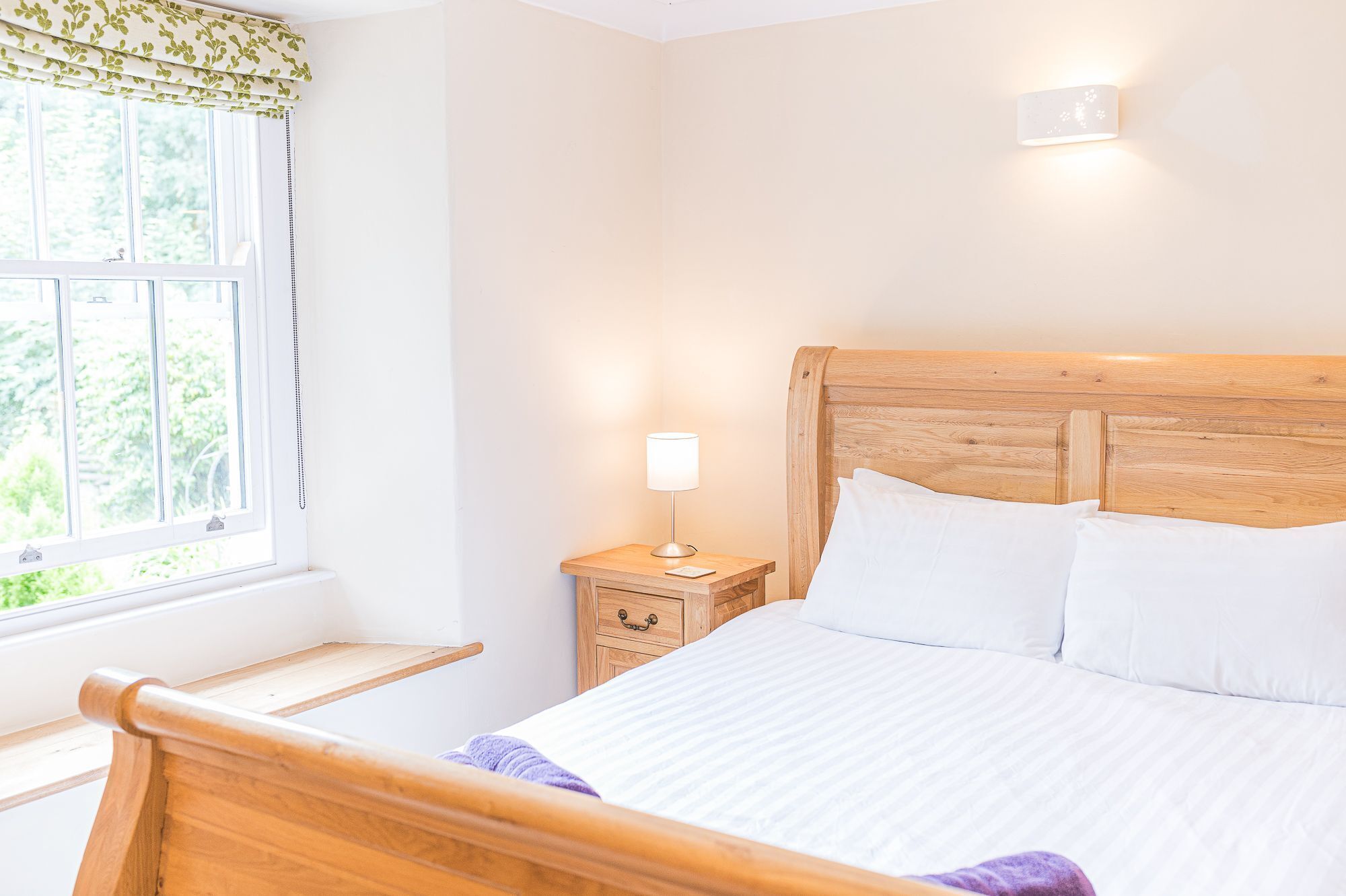 Une chambre à coucher avec une tête de lit en bois, une table de chevet avec une lampe et une fenêtre donnant sur un paysage verdoyant.