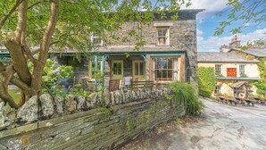 A stone building with a stone wall in front, a bench, and a tree.