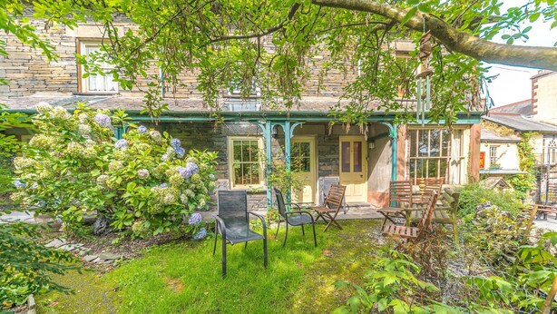 A stone building with a porch, outdoor seating, and a garden with hydrangeas.