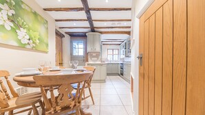 A dining area with a wooden table and chairs, a kitchen with wooden cabinets and a tiled floor, and a wooden door.