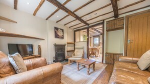 A cozy living room with leather sofas, a fireplace, wooden beams, and a television.