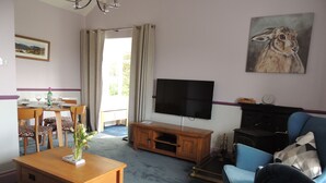 A living room with a TV, a dining table with chairs, a sofa, and a painting on the wall. - Lake District cottage with gorgeous views in Beatrix Potter country (Ambleside)