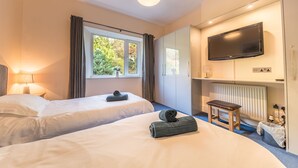A hotel room with two beds, a TV, a window with curtains, a lamp, and a radiator. - Lake District cottage with gorgeous views in Beatrix Potter country (Ambleside)